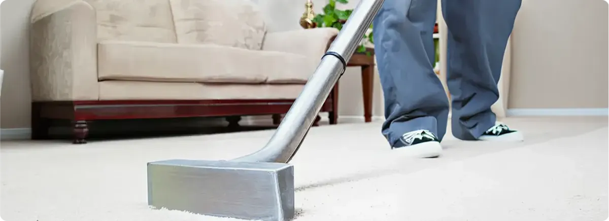 Carpet cleaning technician using a hot-water extraction wand on a light-colored carpet in a living room, Bellevue, WA.
